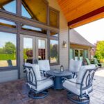 A well-equipped patio with comfortable seating around a central table, enclosed by panoramic windows and doors. Listed by Andi Dyer.