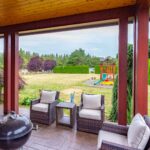 A cozy outdoor lounge area under a protective roof, offering views of a well-appointed yard and play area. Listed by Andi Dyer.