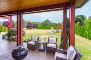 A cozy outdoor lounge area under a protective roof, offering views of a well-appointed yard and play area. Listed by Andi Dyer.